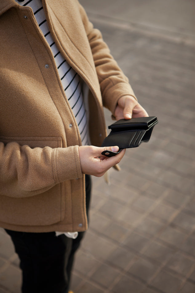 Eine Person hält den schwarzen Cardholder mit Scheinfach Kaktusleder von City Border in der Hand, während sie draußen steht.